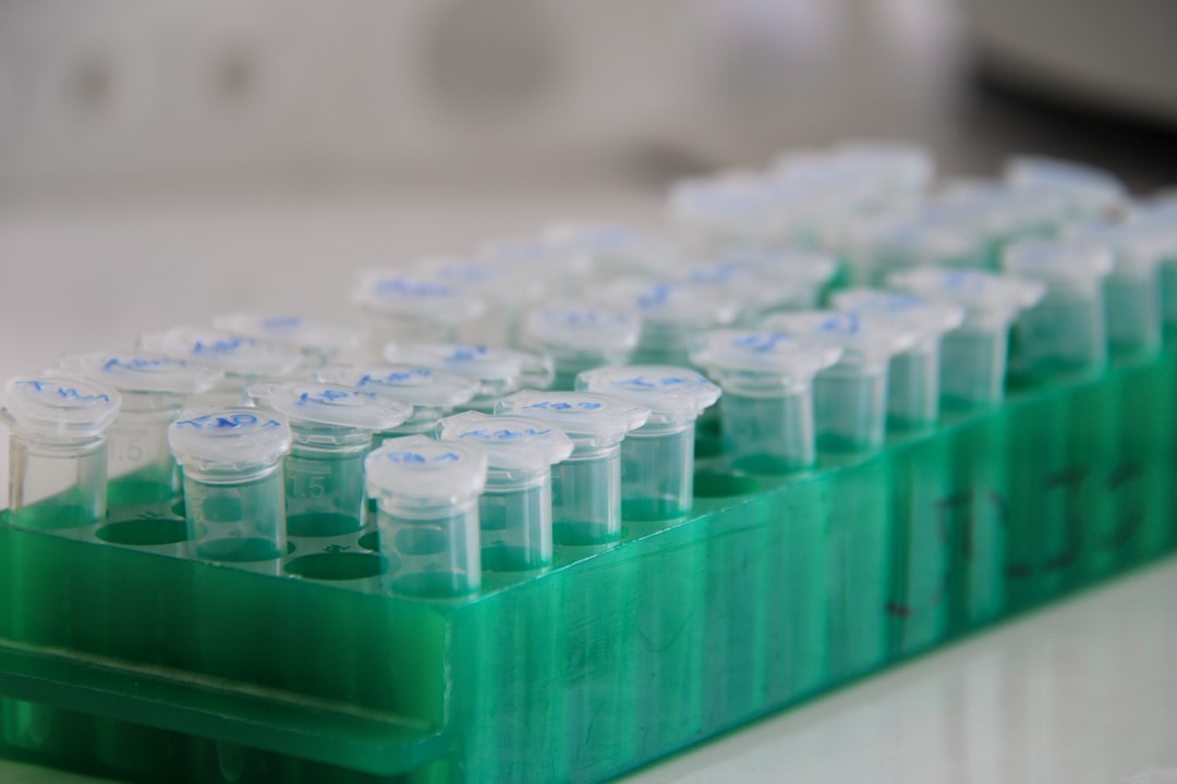 白衣の研究者がピペットで液体を扱う実験風景。がん診断や治療薬の応用開発を象徴する。